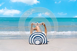 Happy traveler Asian woman lie down to reading a book at tropical beach on vacation. Summer on beach concept