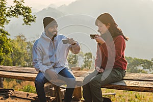 Happy traveler couple resting on mountains in sunrise with drinking coffee