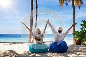 A happy traveler couple sits on bean bags at a tropical beach