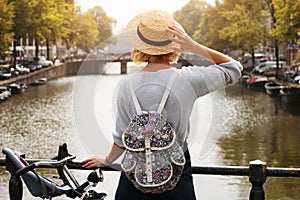 Happy traveler girl enjoying Amsterdam city. Tourist woman looking to the Amsterdam canal, Netherlands, Europe