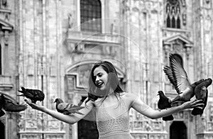 Happy traveler girl in Milan city. Fashion female tourist standing on Piazza Duomo square in Milan. Doves eats feed from