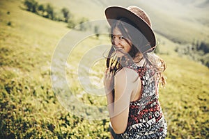 Happy traveler hipster girl in hat, walking in sunny mountains.