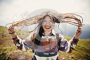 happy traveler hipster girl with windy hair and smiling, standing on top of sunny mountains. space for text. stylish woman waving