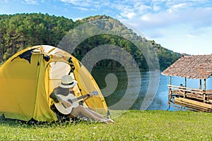Happy traveler lifestyle women on vacation camping with tents playing guitar in the forest near river.