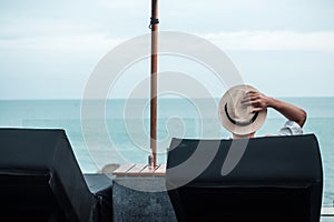 Happy traveler man with hat enjoy beautiful sea view, young man sitting on chair at sand beach. Freedom, relaxing, vacation