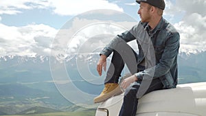 Happy Traveler man sitting on his car on mountains top. 4x4 travel trekking