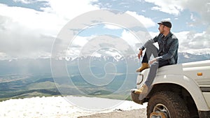 Happy Traveler man sitting on his car on mountains top. 4x4 travel trekking