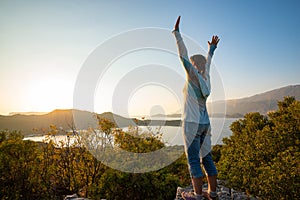 Happy traveler with open arms stands on the rock