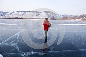 A happy traveler stands on the transparent ice of the frozen Lake Baikal.