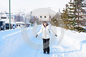 happy Traveler with Sweater and backpack walking on snow covered road in frosty weather, woman tourist sightseeing in Sapporo city