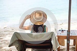 Happy traveler woman in green swimwear and hat enjoy beautiful sea view, young woman sitting on chair at sand beach. Freedom,