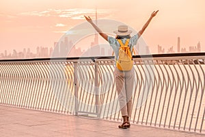 Happy traveler woman with a hat and a yellow backpack enjoys a stunning panoramic view of the Dubai Creek Canal and the famous