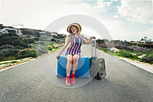 Happy traveler woman sitting on a suitcase on the road and laughs. Concept of travel, journey, trip