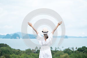 Happy traveler woman in white dress enjoy Beautiful view, alone Tourist with hat standing and relaxing over ocean. travel, summer