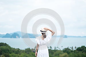 Happy traveler woman in white dress enjoy Beautiful view, alone Tourist with hat standing and relaxing over ocean. travel, summer