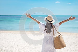 Happy traveler woman in white dress and hat enjoy beautiful sea view, young woman standing on sand and looking ocean at tropical
