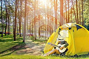 Happy traveler women on vacation camping with tents playing guitar in the forest near river.