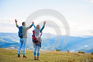 Happy travelers couple conquered top of mountain, raises hands up