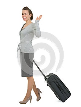 Happy traveling woman with suitcase waving hand
