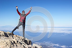 Happy traveller with camera and tripod standing on mountain peak with hands up