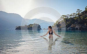 Happy traveller woman in black swimsuit enjoys her tropical beach vacation