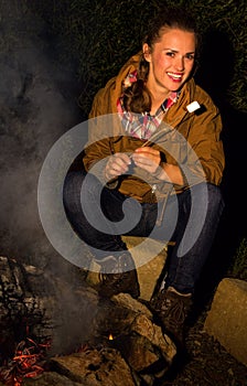 Happy traveller woman by camping fire with roasted marshmallow