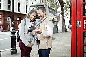 Happy travelling couple reviewing photos in London, UK. Double decker bus and red telephone booth in a frame