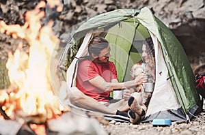 Happy trekker couple camping tent with dog next bonfire - Hipster man and woman having fun mountaineering together