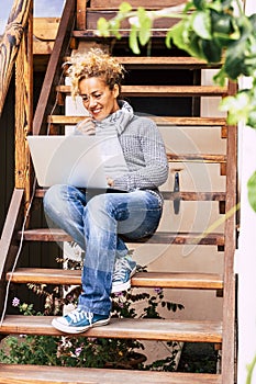 Happy trendy caucasian beautiful woman use online computer with internet connection to work in the garden at home like an