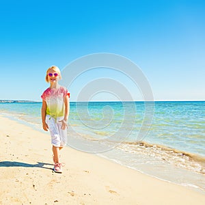 Happy trendy girl in colorful shirt on seacoast walking