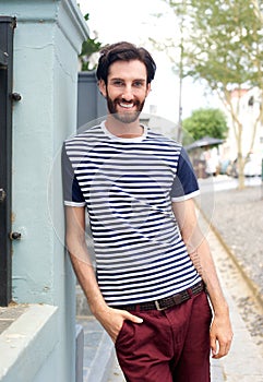 Happy trendy man in striped shirt leaning against wall outdoors