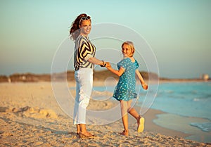 Happy trendy mother and child on seacoast at sunset