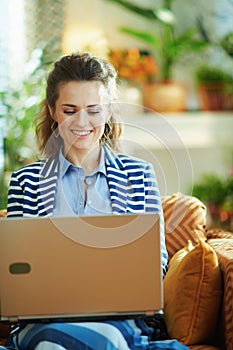 Happy trendy woman with laptop in modern house in sunny day