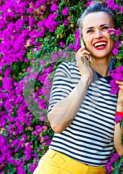 Happy trendy woman near flowers bed talking on cell phone