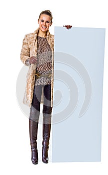 Happy trendy woman in winter coat on white showing blank board