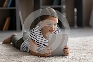 Happy tween girl child lying on carpet using digital touchpad