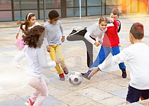 Happy tween girls and boys playing football in schoolyard