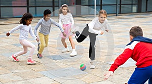 Happy tween girls and boys playing football in schoolyard