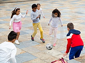 Happy tween girls and boys playing football in schoolyard