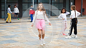 Happy tweenager girl skipping rope in schoolyard