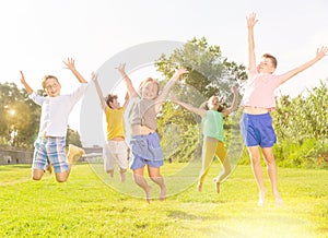 Happy tweenagers jumping on green lawn on summer day