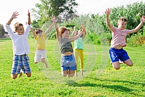 Happy tweenagers jumping on green lawn on summer day