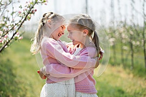 Happy twin sisters hug against the background of a green blooming Apple orchard.