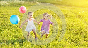 Happy twin sisters running around laughing and playing with balloons in summer