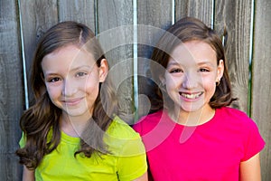 Happy twin sisters smiling on wood backyard fence