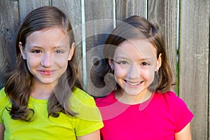 Happy twin sisters smiling on wood backyard fence