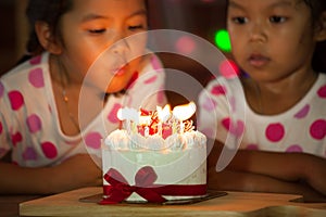 Happy twin two asian little girls blowing candles on birthday cake