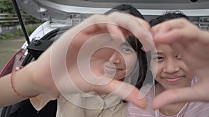 Happy two Asian teen sisters making hand gesture heart shape and smiling while looking at camera.