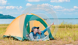 Happy two Asian woman lying down in the tent while camping on meadow near a lake in parks and outdoor on vacation
