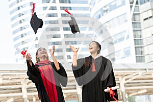 Happy two Asian young beautiful graduate female students with master and bachelor degree throwing cap to the sky after graduation